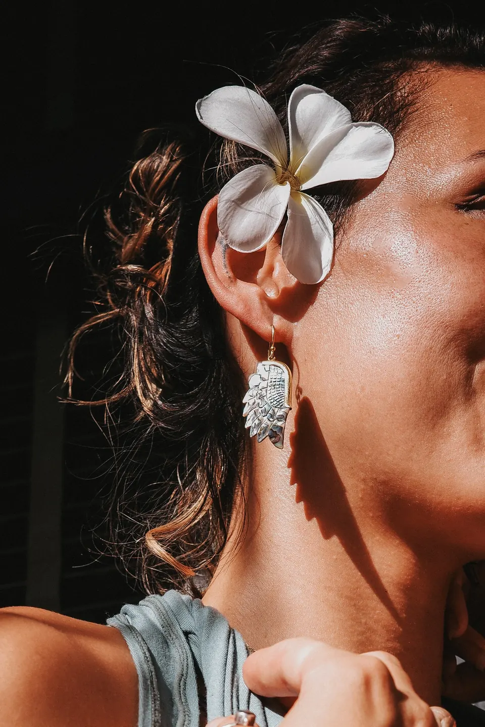 Nahaufnahme einer Frau mit weißer Blüte im Haar und silbernem Ohrring