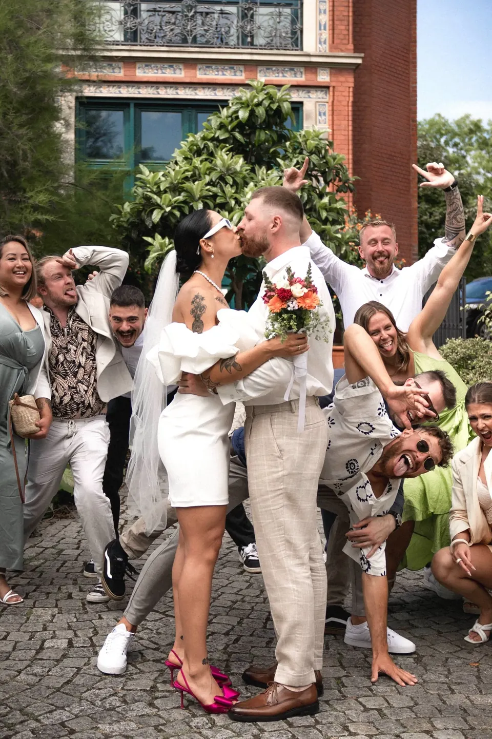 Brautpaar küsst sich, Freunde jubeln ausgelassen um sie herum